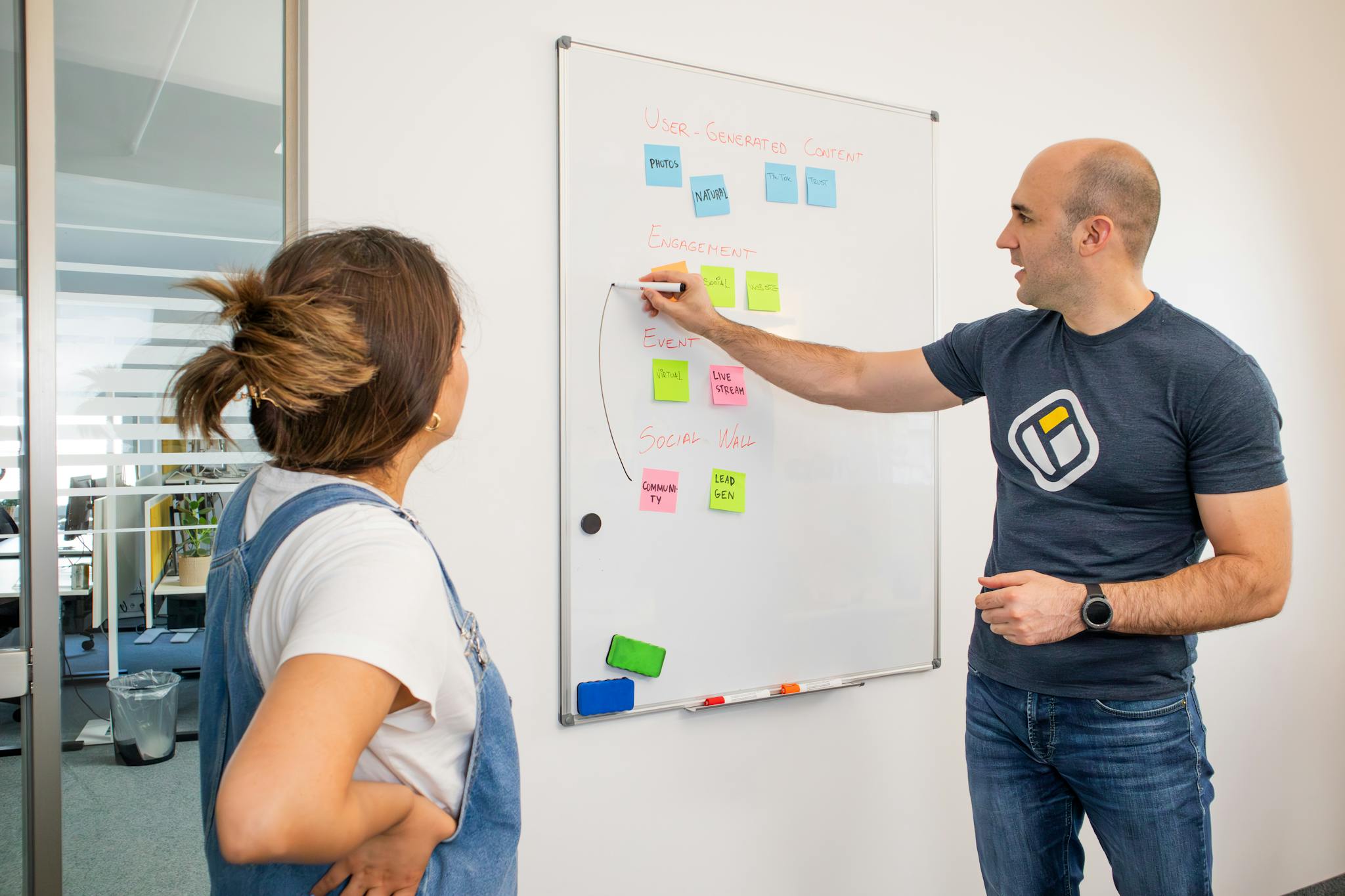 Two colleagues brainstorming marketing strategies on a whiteboard.