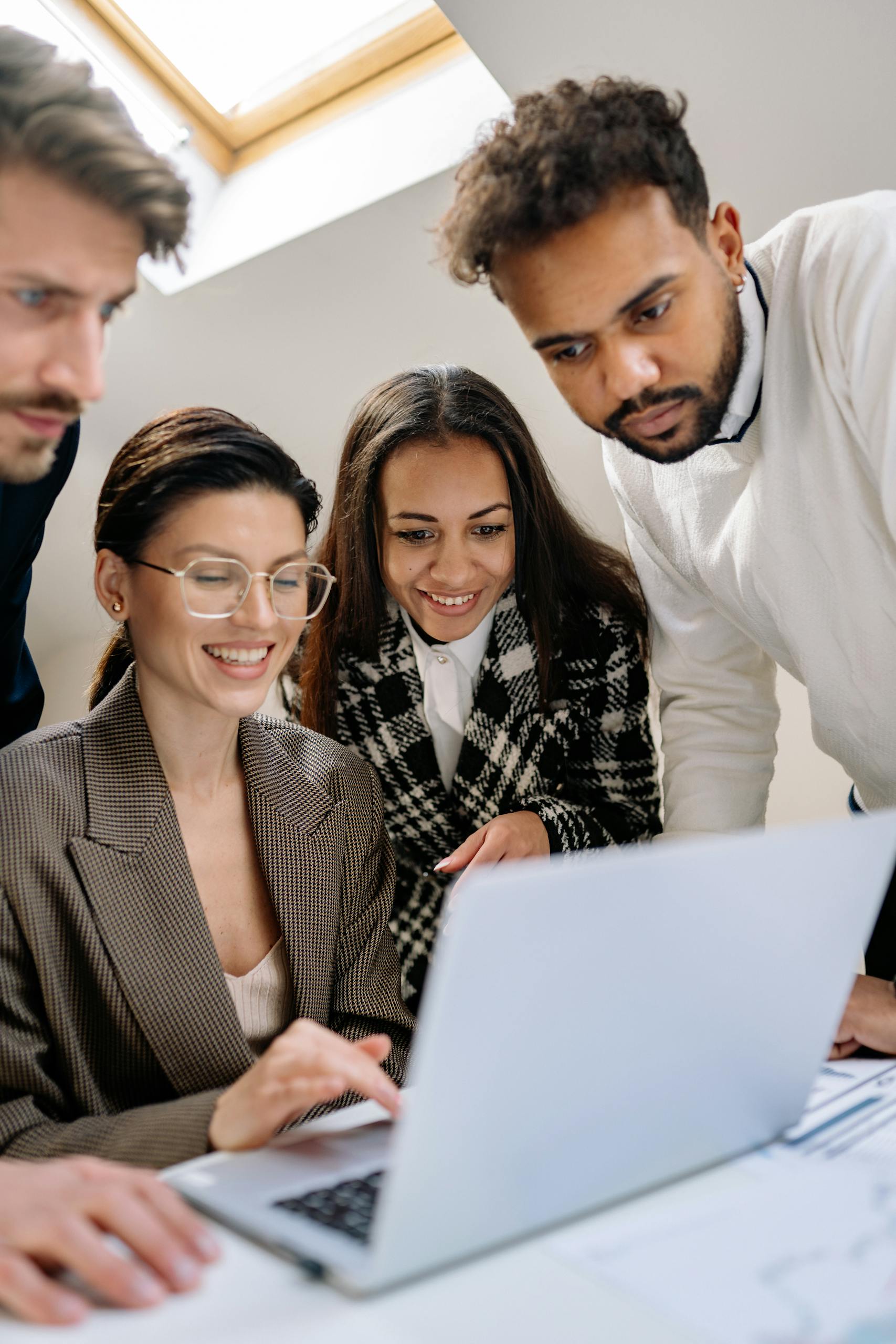 A diverse team of professionals happily collaborating on a laptop at the office.