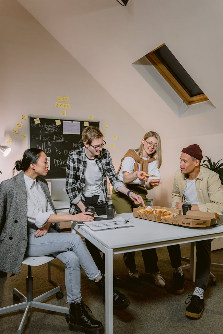 A group of diverse young professionals sharing pizza during a break in a modern office environment.